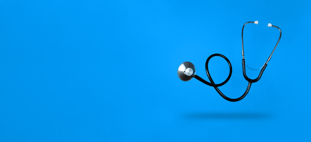 Levitating stethoscope on blue background and shadow under it with copy space. Stock photo. - Photo, Image