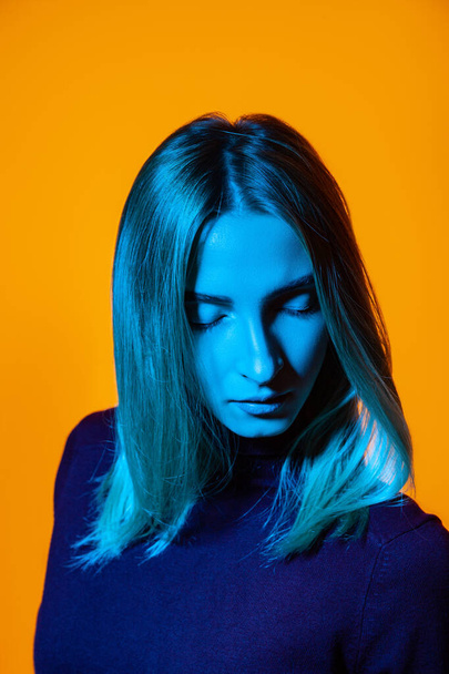 Pensive młoda kobieta z zamkniętymi oczami w jasnym studio z niebieskim oświetleniem - Zdjęcie, obraz