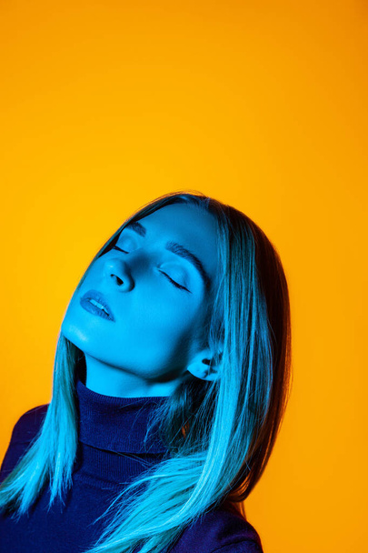 Pensive young woman with closed eyes in bright studio with blue illumination - Фото, изображение