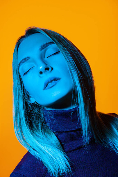 Pensive young woman with closed eyes in bright studio with blue illumination - Foto, Imagem