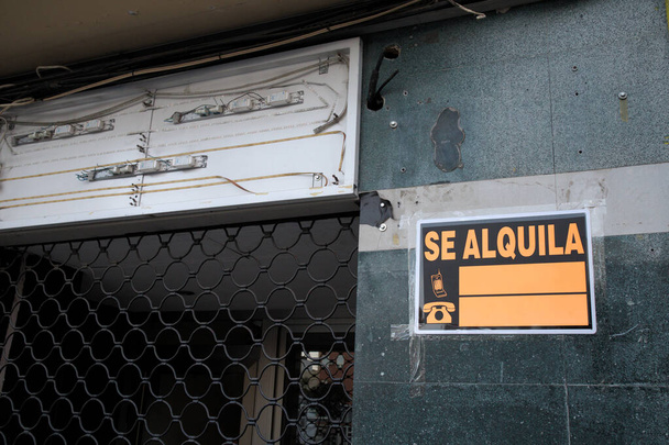 Close-up van een winkelgevel met de rolluiken gesloten en een bord dat aangeeft dat de plaats te huur is geschreven in het Spaans (Se Alquila) en ruimte om een telefoonnummer toe te voegen - Foto, afbeelding