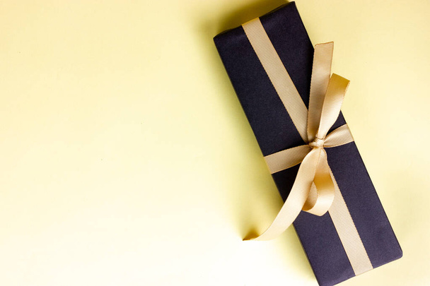 Black gift tied with a beige ribbon on a yellow background. View from above. - Foto, Bild