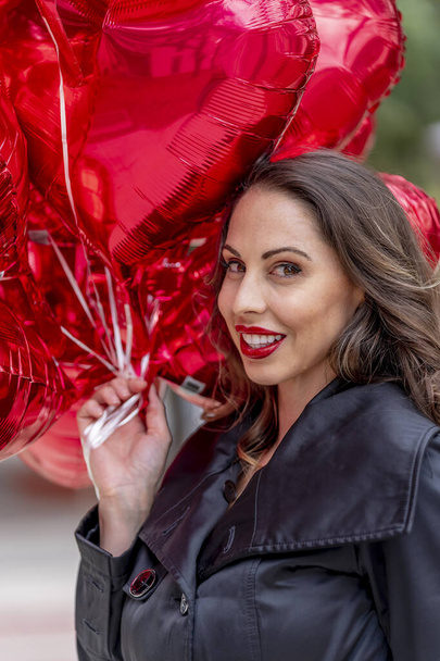 ein schönes brünettes Model mit einem Dutzend Luftballons zum Valentinstag - Foto, Bild