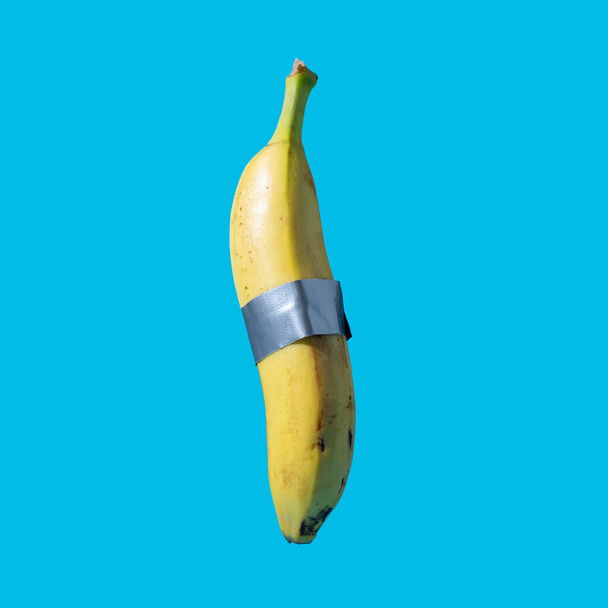 Banán osztott művészeti koncepció vágott gyümölcs tartja össze ragasztószalaggal. Elszigetelve a kék háttér minimális kreatív ötlet. - Fotó, kép