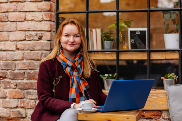 Houkutteleva nuori tyylikäs liiketoiminnan nainen viettää aikaa kahvilassa, juo kahvia ja työskentelee hänen kannettavan tietokoneen. Romanttinen naisbloggaaja ikkunan lähellä ulkona. Freelancer ajattelee uusia ideoita. - Valokuva, kuva