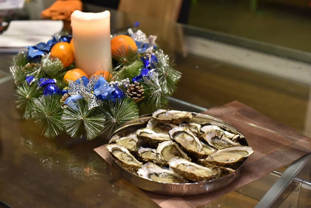 Bord van oesters op kersttafel versierd met kaarsen en sparren takken - Foto, afbeelding