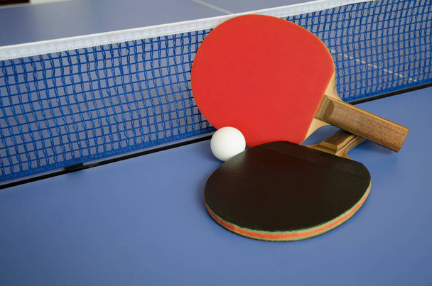 Red and black Table Tennis Paddles and ball on the blue table tennis table with net. Ping Pong concept with copy space - Photo, image