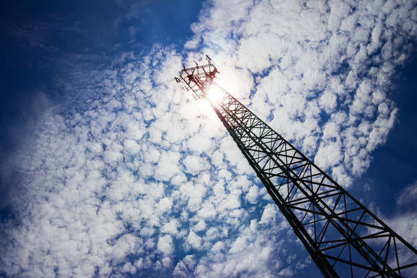 Una antena de telecomunicaciones muy alta con una vista de ángulo de abajo hacia arriba y una perspectiva evidente desde el suelo, con un día soleado y un fondo de cielo azul y bengalas de lentes - Foto, Imagen