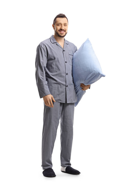 Full length portrait of a young man in pajamas holding a pillow and smiling at camera isolated on white background - Foto, Imagen