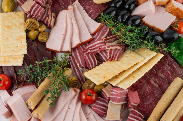 Ein Teller mit verschiedenen Fleischprodukten, Oliven, Brot, Kräutern. Blick von oben. - Foto, Bild