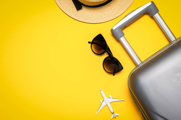 Zomer achtergrond hout. Dames accessoires reiziger: koffer, wit vliegtuig, zonnebril op gele achtergrond met lege ruimte voor tekst. Bovenaanzicht, vlak. Kopieerruimte - Foto, afbeelding