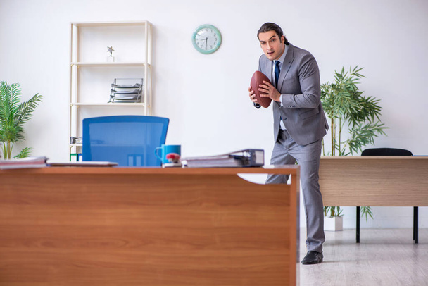 Joven empleado masculino con pelota de rugby en la oficina - Foto, Imagen