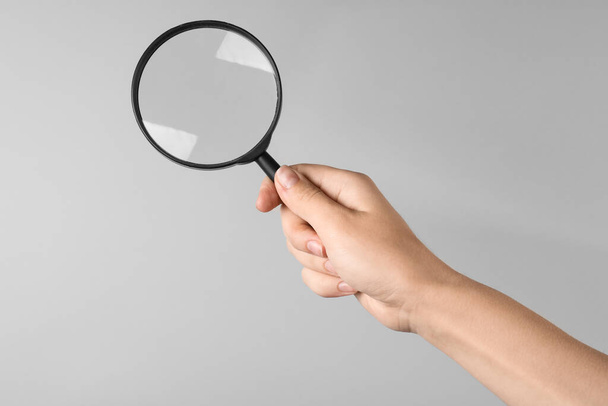 Woman holding magnifying glass on grey background, closeup. Find keywords concept - Foto, Imagem