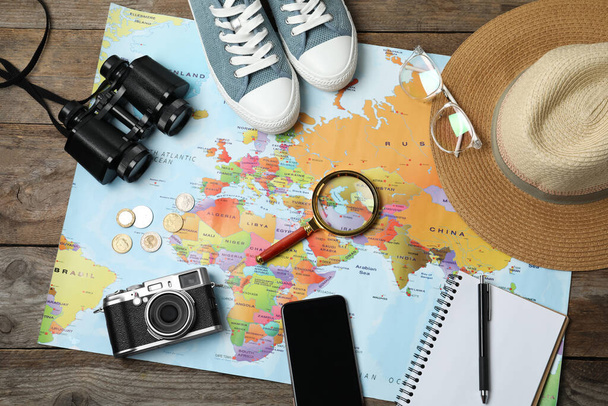 Flat lay composition with world map and different travel accessories on wooden table. Planning summer vacation trip - 写真・画像