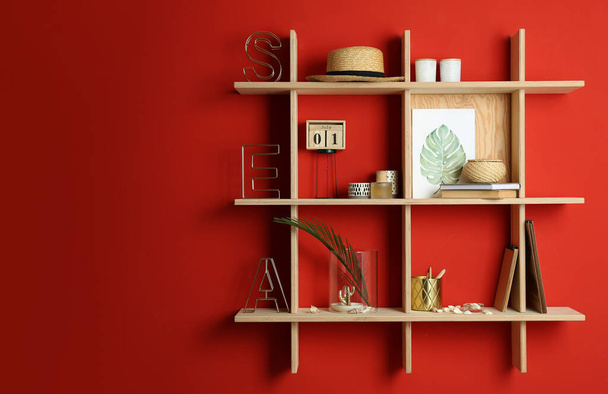 Stylish wooden shelves with decorative elements on red wall. Space for text - Фото, изображение