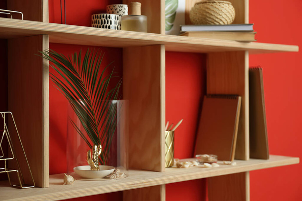 Stylish wooden shelves with decorative elements on red wall - Φωτογραφία, εικόνα