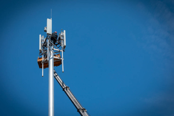 Рабочие устанавливают сотовую базовую станцию с передатчиками 3G, 4G, 5G и антенны на сотовой вышке на фоне голубого неба. Мобильное телекоммуникационное оборудование. Копирование пространства - Фото, изображение