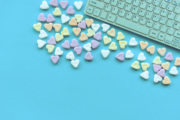 Veelkleurige hartvormige snoepjes en toetsenbord op een turquoise achtergrond. Valentijnsdag, concept van liefde. Bovenaanzicht, flat lay, kopieerruimte. - Foto, afbeelding
