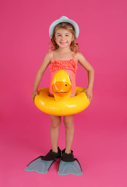 Cute little child in beachwear with bright inflatable ring on pink background - Foto, afbeelding