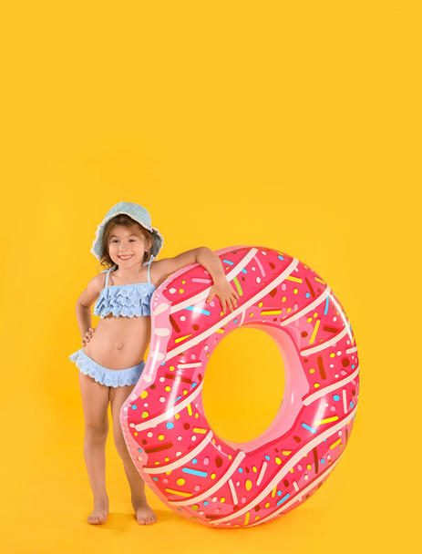 Cute little child in beachwear with bright inflatable ring on yellow background - Photo, Image