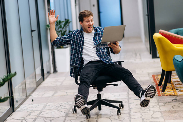Sandalyede oturan aşırı mutlu erkek çalışan dizüstü bilgisayar ekranına bakıp gülümsüyor. Beyaz iş adamı iyi haberler okuyor, başarılı bir proje ya da başlangıç için mutlu. İyi iş konsepti - Fotoğraf, Görsel