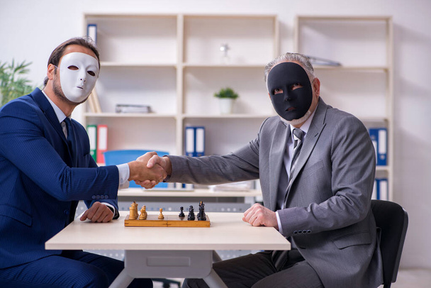 Двое бизнесменов играют в шахматы в масках - Фото, изображение