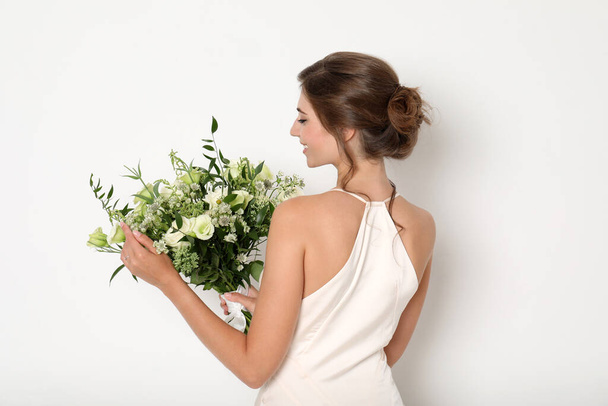 Young bride wearing wedding dress with beautiful bouquet on light background - Φωτογραφία, εικόνα