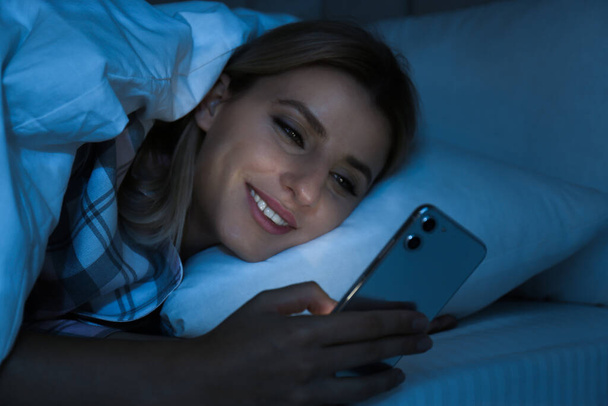 Young woman using smartphone in bed at night. Nomophobia and sleeping disorder problem - Fotografie, Obrázek
