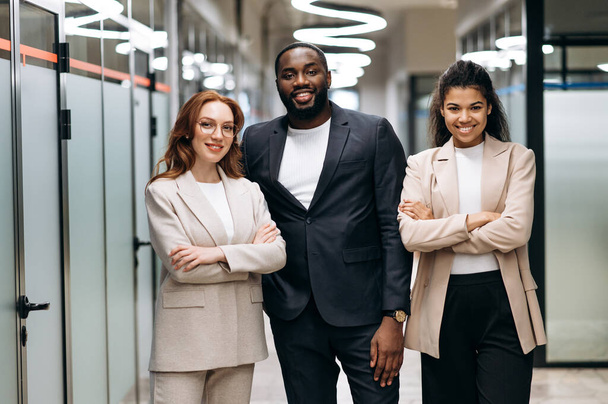 Multiracial influential business people in formal wear look at the camera, smiling. Happy female and male colleagues stand in modern office, show confidence and success, teamwork concept - Photo, Image