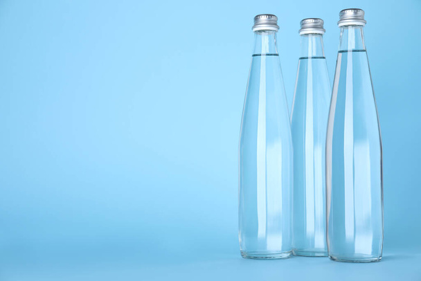 Glass bottles with water on light blue background, space for text - Foto, Bild