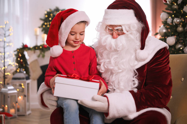 Santa Claus giving present to little girl in room decorated for Christmas - Photo, Image