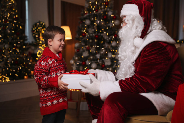Santa Claus giving present to little boy in room decorated for Christmas - Фото, зображення