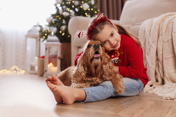 Cute little girl with English Cocker Spaniel in room decorated for Christmas - Фото, изображение