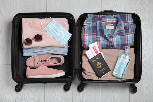 Открытый чемодан с паспортом, билетами, антисептиком и защитной маской на деревянном полу, вид сверху. Путешествие во время карантина - Фото, изображение