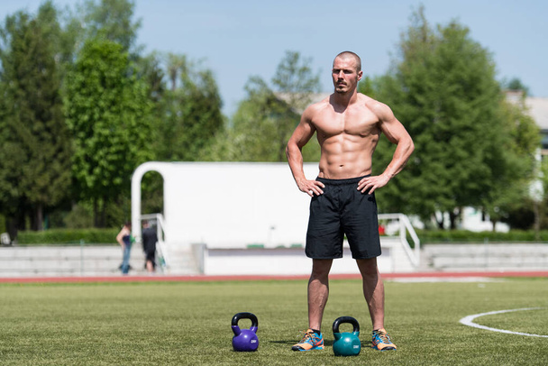 Man Exercising With Kettle Bell Outdoor and Flexing Muscles - Muscular Athletic Bodybuilder Fitness Model Exercises - Photo, image