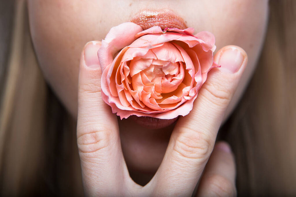 口の中にバラの花を持つ美しい若い女性。美とファッション. - 写真・画像