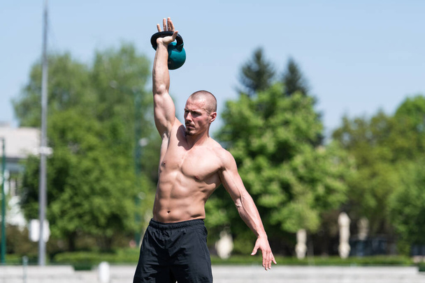 Man uit te werken met ketel bel buiten - Bodybuilder doet zware gewicht oefening met Waterbel - Foto, afbeelding