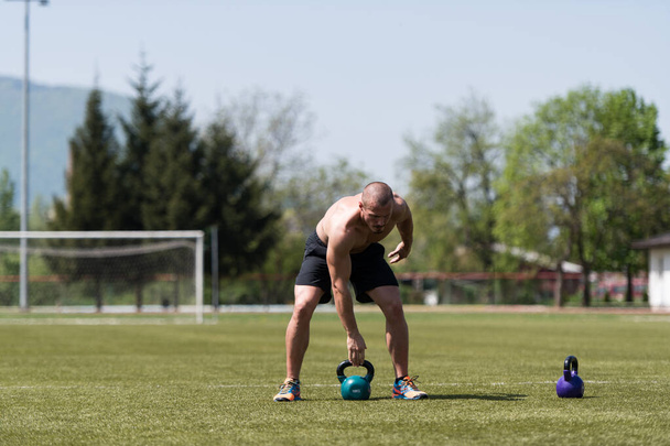 Mies käyttää vedenkeitin Bell ulkona ja taivutus lihakset - Lihaksikas urheilullinen kehonrakentaja Fitness Malli harjoitukset - Valokuva, kuva