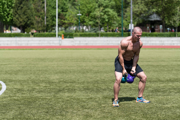 Man Exercising With Kettle Bell Outdoor and Flexing Muscles - Muscular Athletic Bodybuilder Fitness Model Exercises - Valokuva, kuva