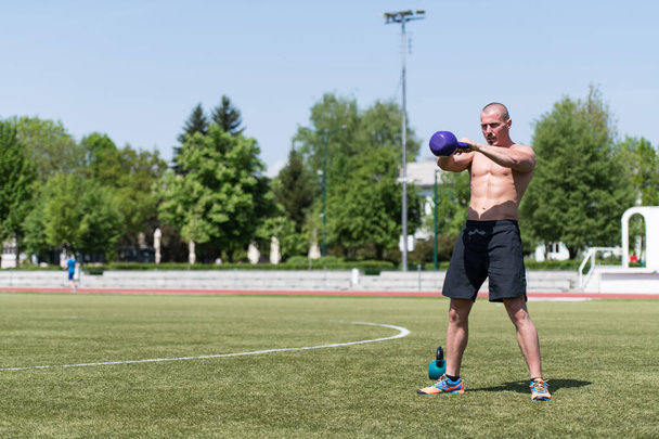 Man Exercising With Kettle Bell Outdoor and Flexing Muscles - Muscular Athletic Bodybuilder Fitness Model Exercises - 写真・画像