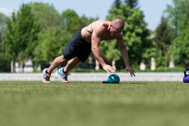 Healthy Man Athlete Doing Pushups Workout With Kettle Bell Outdoor - Kettle-bell Exercise - Foto, Bild