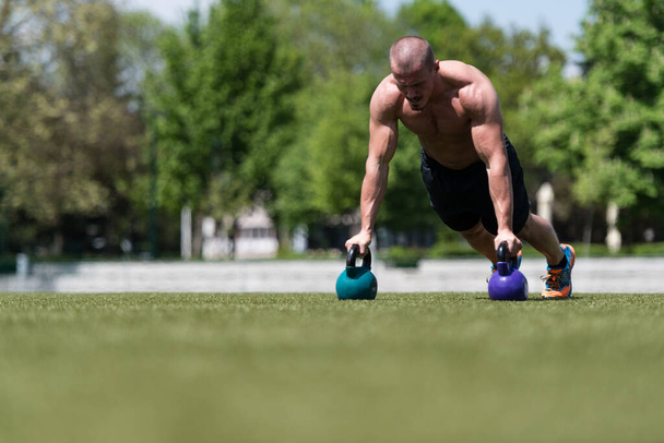 Healthy Man Athlete Doing Pushups Workout With Kettle Bell Outdoor - Kettle-bell Exercise - Foto, afbeelding
