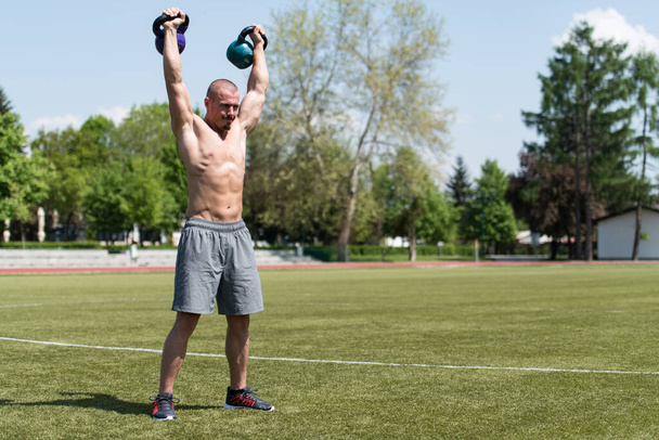 Man Exercising With Kettle Bell Outdoor and Flexing Muscles - Muscular Athletic Bodybuilder Fitness Model Exercises - Foto, immagini