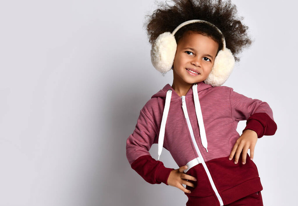 Happy smiling African American girl posing in warm headphones and sportswear. - Foto, imagen
