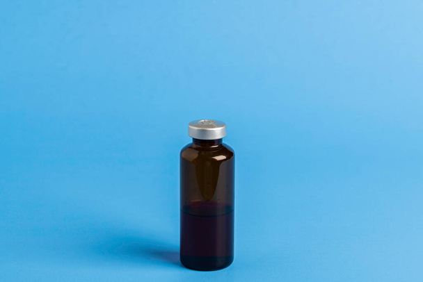 Makro snímek s selektivním zaměřením jantarové barvy vakcíny injekční lahvička nastavena na jednoduchém modrém pozadí. - Fotografie, Obrázek
