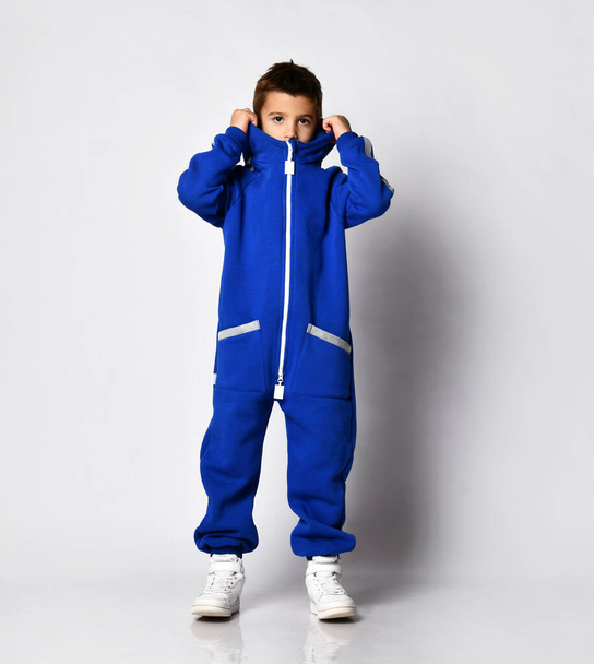Boy dressed in a stylish blue tracksuit and white sneakers posing on a white background. - Photo, image