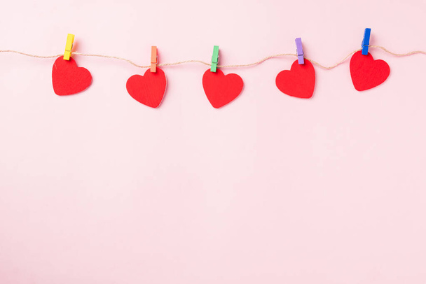 Happy Valentine's day background. red heart shaped valentines decoration hanging with paper clips on the rope for love composition greeting card isolated on pink background with copy space - 写真・画像