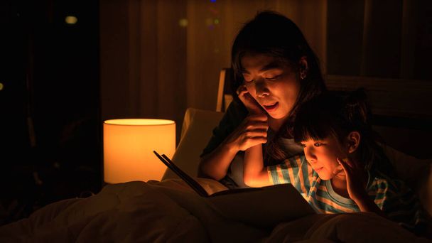 asian mom and daughter having goodtime together mom read bedtime stories fairytale for child on bed before getting to sleep. concept of mother and daughter relationship - Fotografie, Obrázek