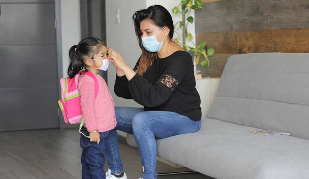 mamma latina e bambina di 3 anni con maschere protettive e zaino per il ritorno a scuola, nuovo covid-19 normale - Foto, immagini