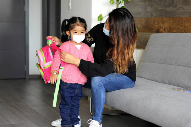 latin mom and 3 year old girl with protective face masks and backpack for back to school, new normal covid-19 - Fotoğraf, Görsel